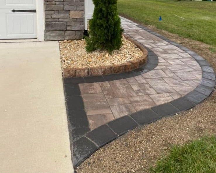 A brick walkway leading to a house with a tree in the middle of it.
