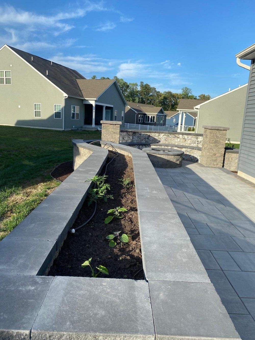 A patio with a planter in the middle of it and a house in the background.