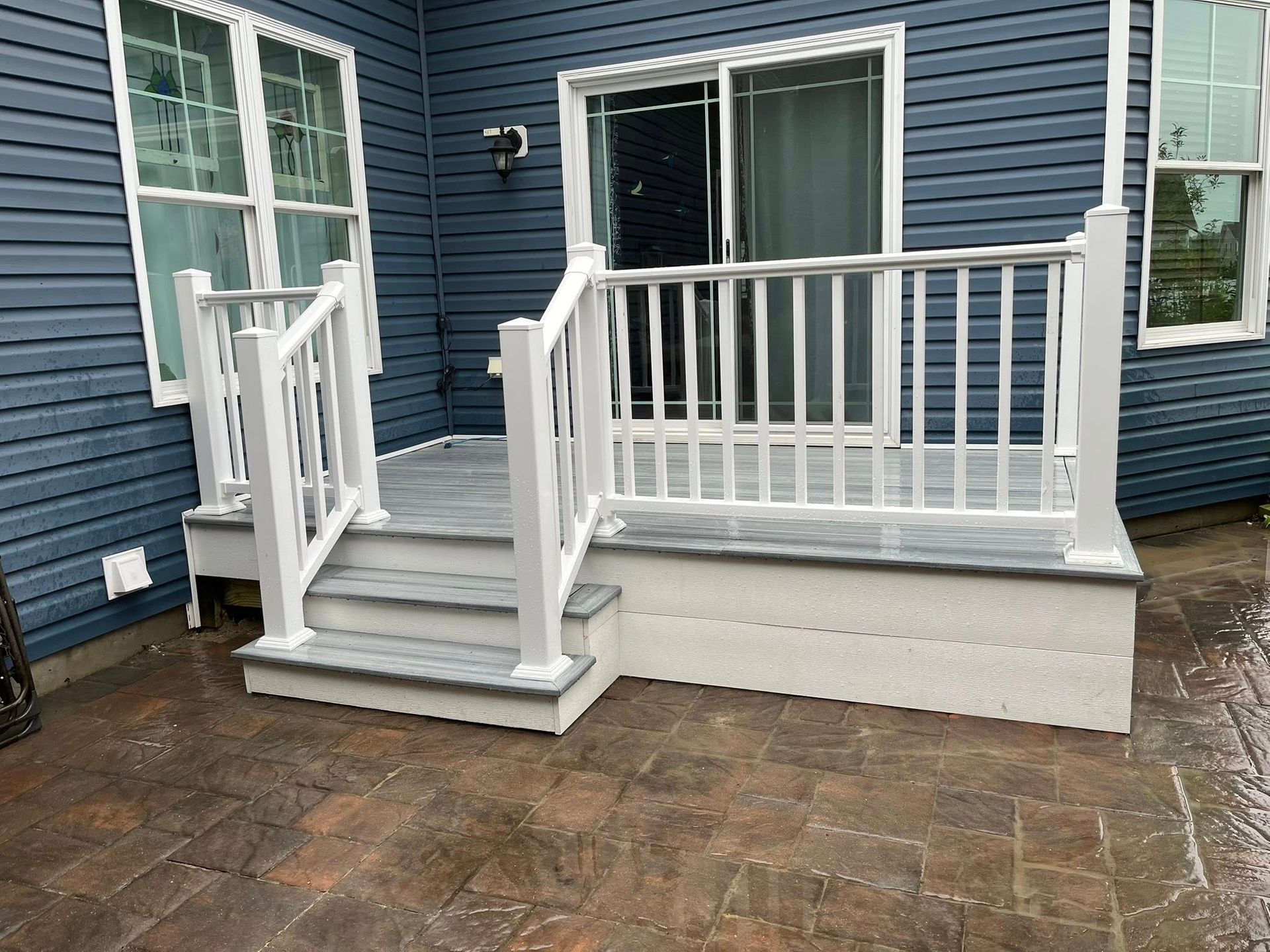 A porch with a white railing and stairs in front of a blue house.