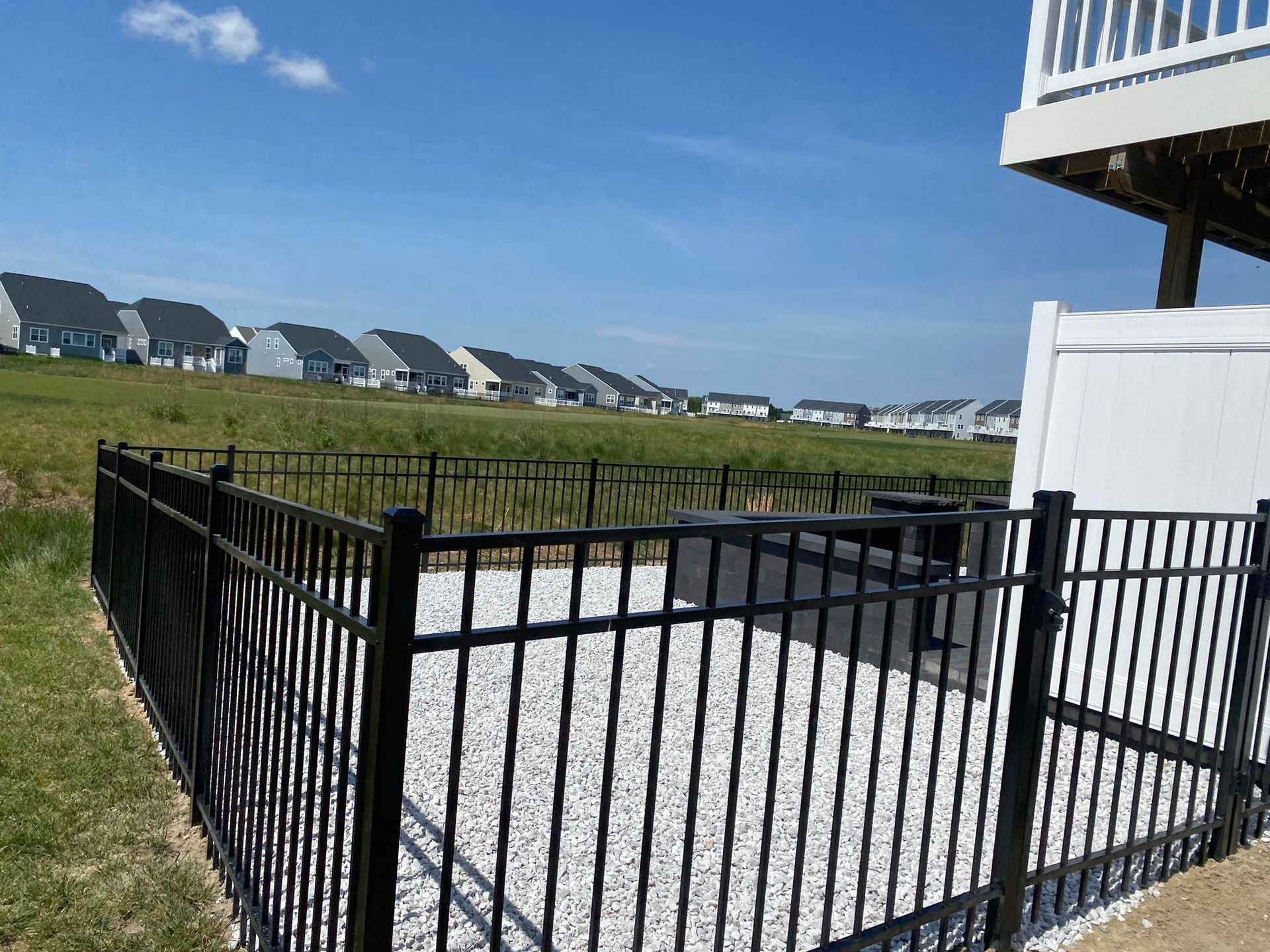 A black fence surrounds a gravel area in front of a house.