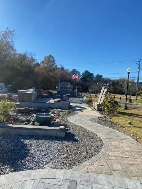 Curved stone path through a landscaped garden with benches, rocks, and an American flag under a clear blue sky
