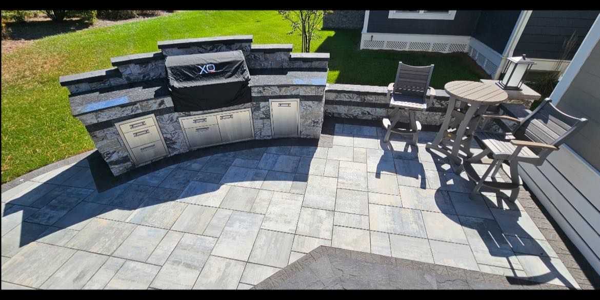 Outdoor patio with built-in stone grill, curved seating wall, and dining table on paved patio