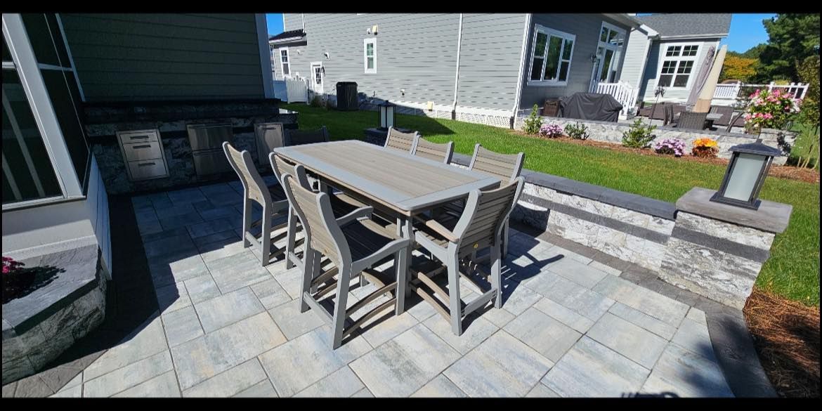 Patio with gray stone pavers, wooden table and chairs, and a small raised garden bed beside a house