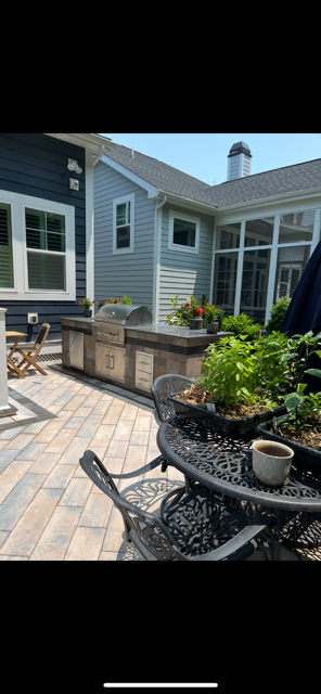 Back patio with gray siding, potted flowers, wicker chairs, and a paved stone floor