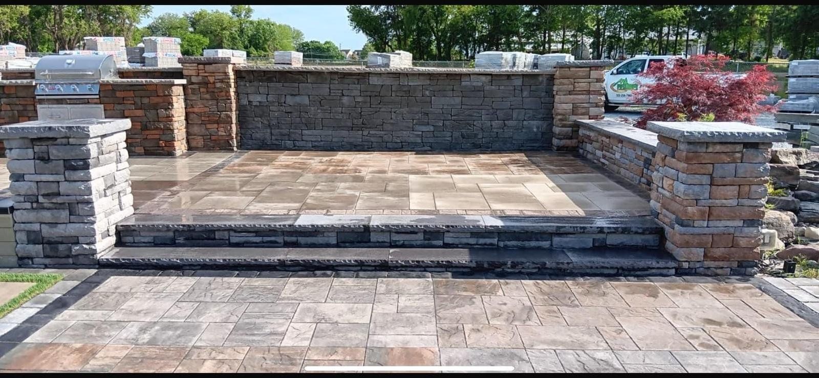 Stone patio with steps leading to a raised brick-and-stone seating area in a landscaped backyard