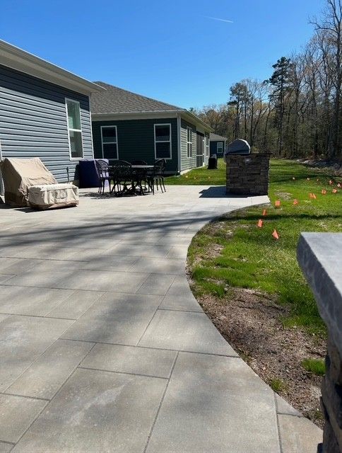 Patio beside a house with outdoor furniture, a brick fire pit, and a grassy yard on a sunny day