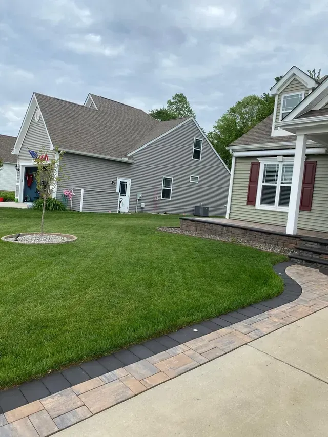 Suburban house with gray siding, green lawn, and curved stone walkway beside a driveway