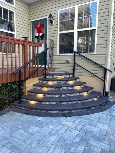Curved front steps with lit stair lights, black railings, and a holiday wreath on the door next to a house entry