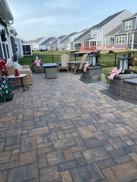 Backyard patio with stone pavers, seating, potted plants, and a row of houses in the background