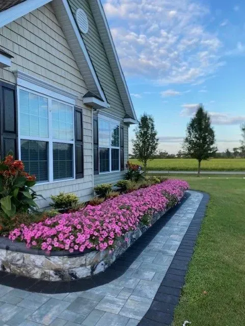 House exterior with large windows, pink flower bed, and gray stone edging beside a green lawn