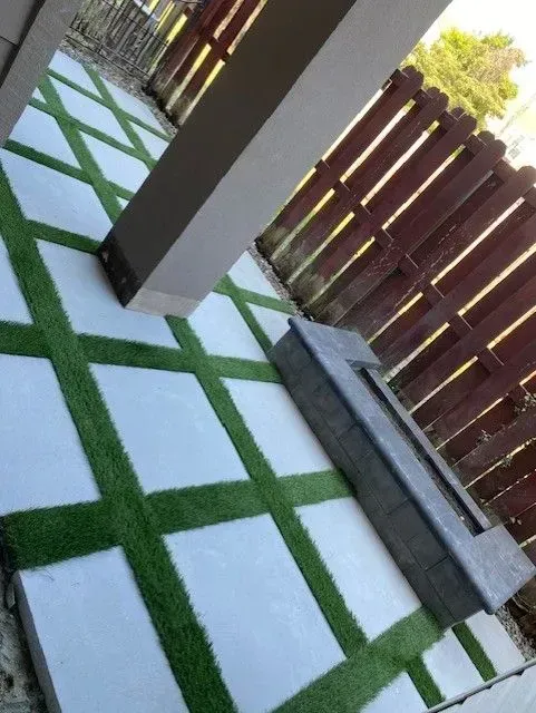 Outdoor patio with white-and-green tiled flooring, a wooden fence, and a concrete bench beside a pillar.