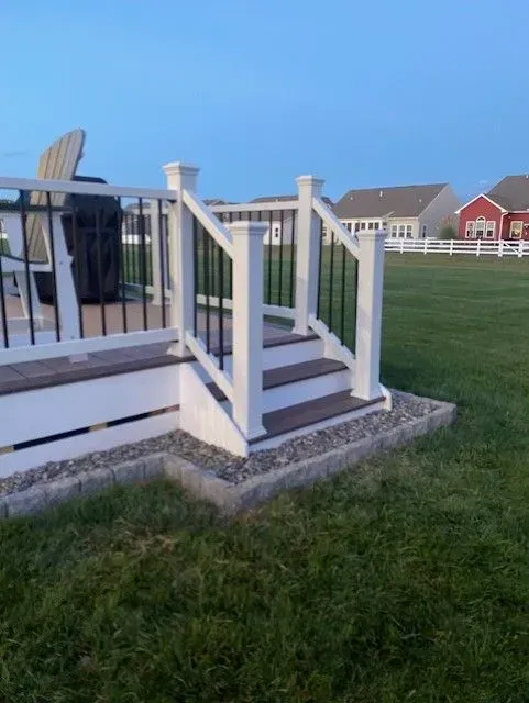 White-railed porch stairs with gray steps beside a grassy yard at dusk