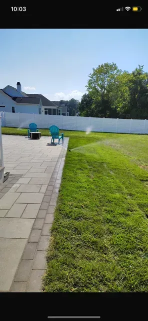 Backyard patio with blue chairs, green lawn, and a white fence under a clear sky