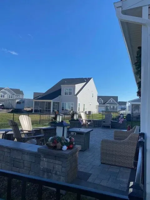 Patio with wicker chairs, fire pit, and flower planter overlooking suburban houses under a clear blue sky