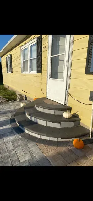 Yellow house entrance with black-and-white curved steps, white door, and a small pumpkin on the walkway