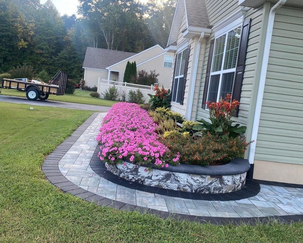Curved stone flower bed with pink blooms beside a house and lawn at dusk
