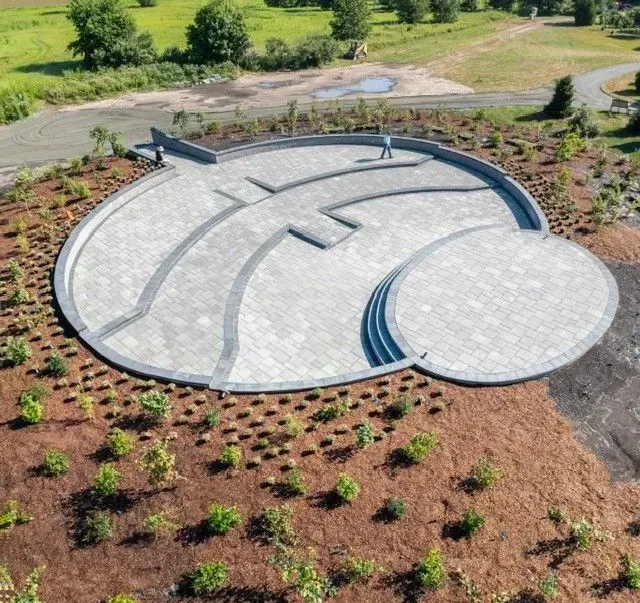 Circular stone patio design in a landscaped garden, with gray pavers and curved sections on a slope.