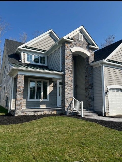 Suburban house with gray siding, white trim, stone entry, and attached garage under a blue sky