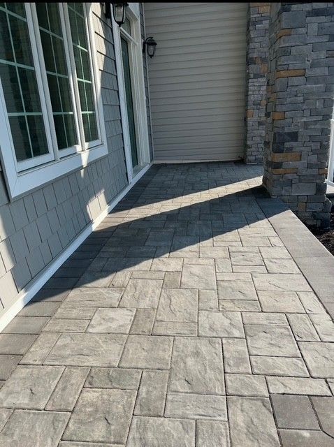 Stone-tile patio walkway beside a house, leading to a covered entry and stone wall.