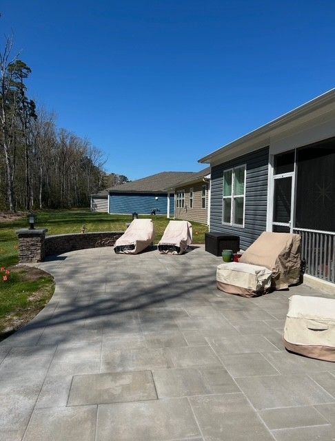 Patio with gray pavers and covered outdoor chairs beside a house under a clear blue sky