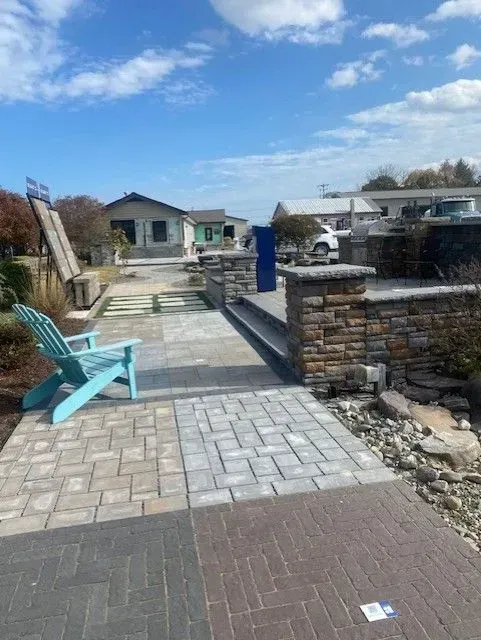 Patio with stone pavers, blue chairs, and a low stone wall under a partly cloudy sky
