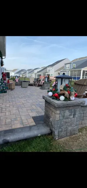Townhouse walkway with paver patio, stone planter of red and green flowers, and row of homes on a sunny day