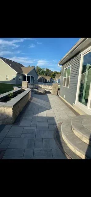 Modern house patio with gray stone walkway, low planter wall, and blue sky over a residential courtyard