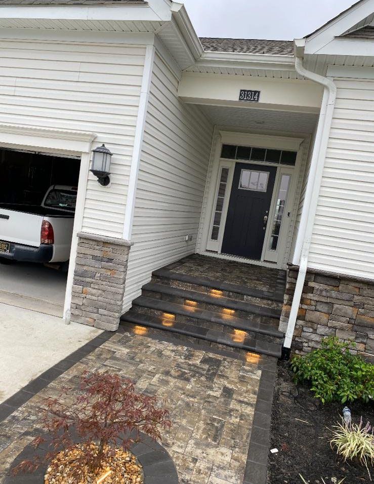 Front walkway and steps leading to a house entrance, with stone siding and a partially open garage.