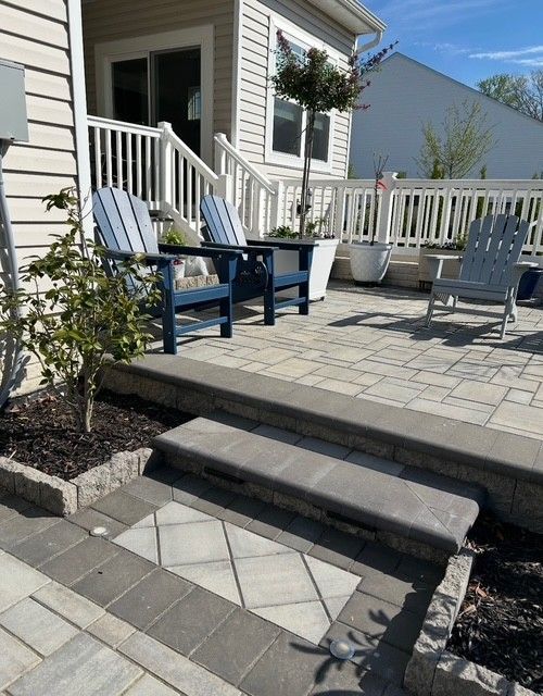 Front patio with white chairs, blue table, potted plants, and two steps leading to a paved walkway.