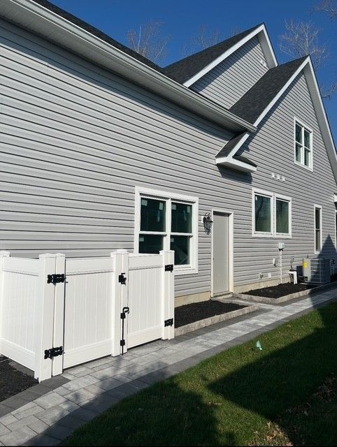 Gray house exterior with white fence, windows, and green lawn under a blue sky