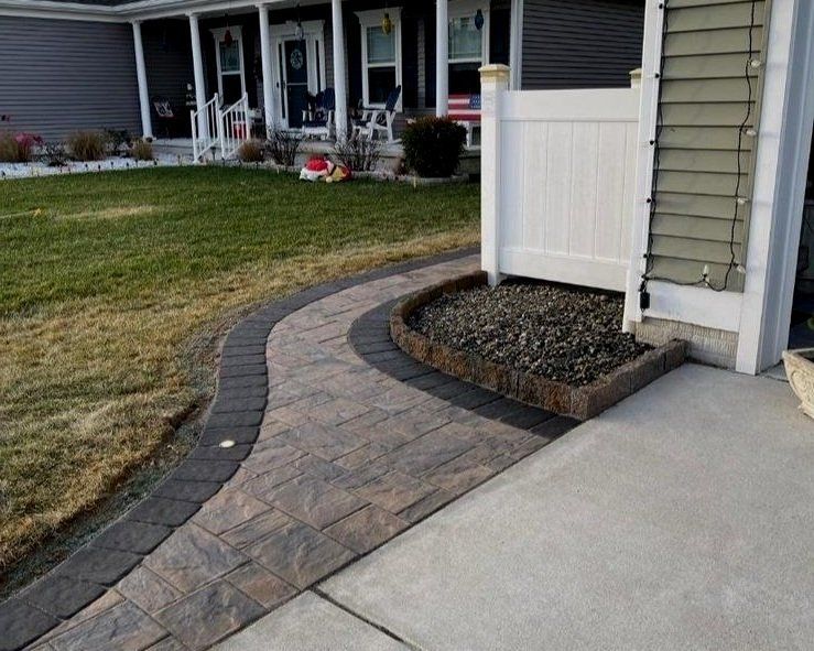 Curved brick walkway leading to a front porch beside a driveway and landscaped mulch bed.