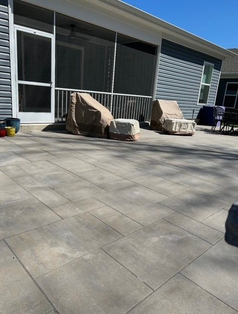 Patio with gray pavers, covered outdoor chairs, and a house sliding door in bright sunlight