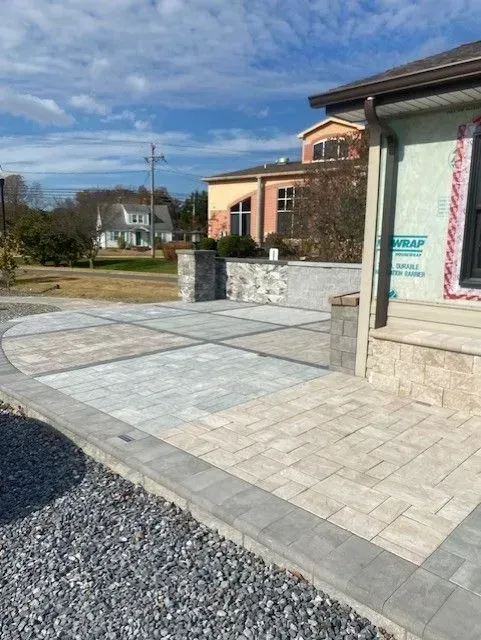 Stone-paved courtyard outside a modern building, with a gravel path and houses in the distance
