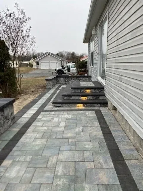 Gray stone patio and steps beside a house, with dark border tiles and yellow step lights