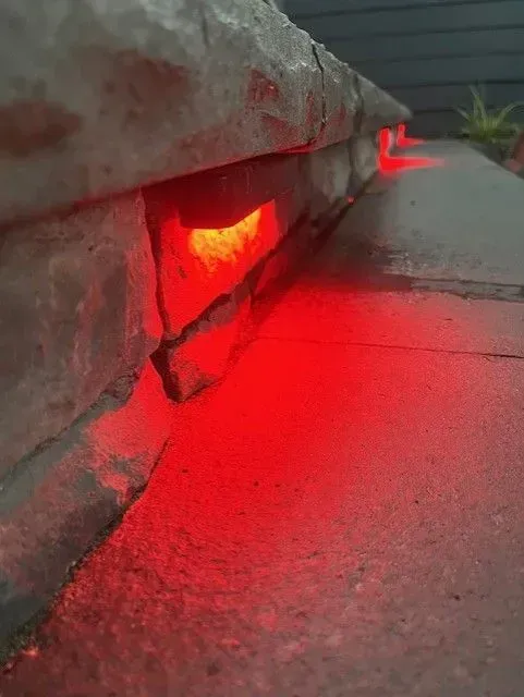 Red LED light glowing beneath a concrete curb at dusk