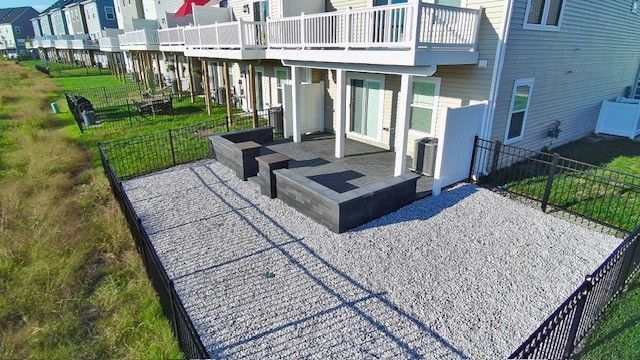 Apartment patio with black seating, gravel ground, and fenced yard beside a white balcony