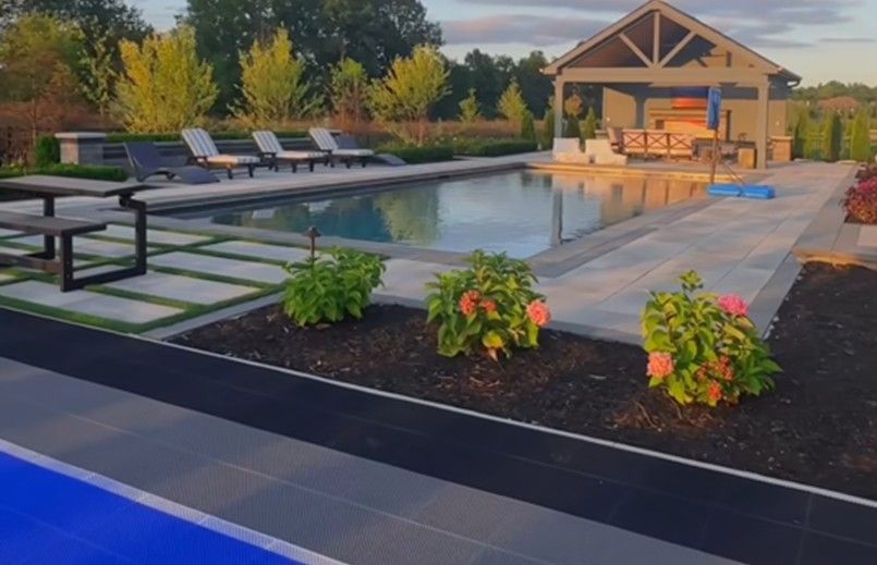 Backyard pool patio with lounge chairs, pavilion, and landscaped flower beds at sunset