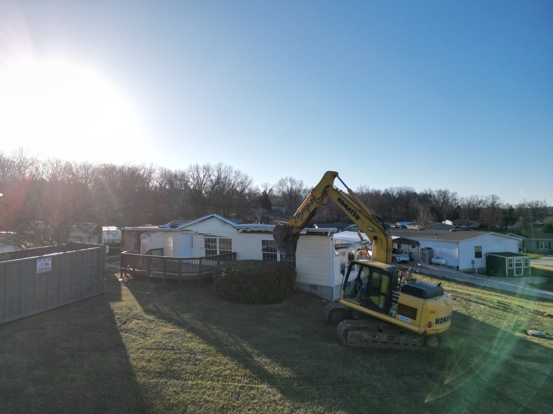Yellow excavator beside a white tank at a construction site in bright sunlight