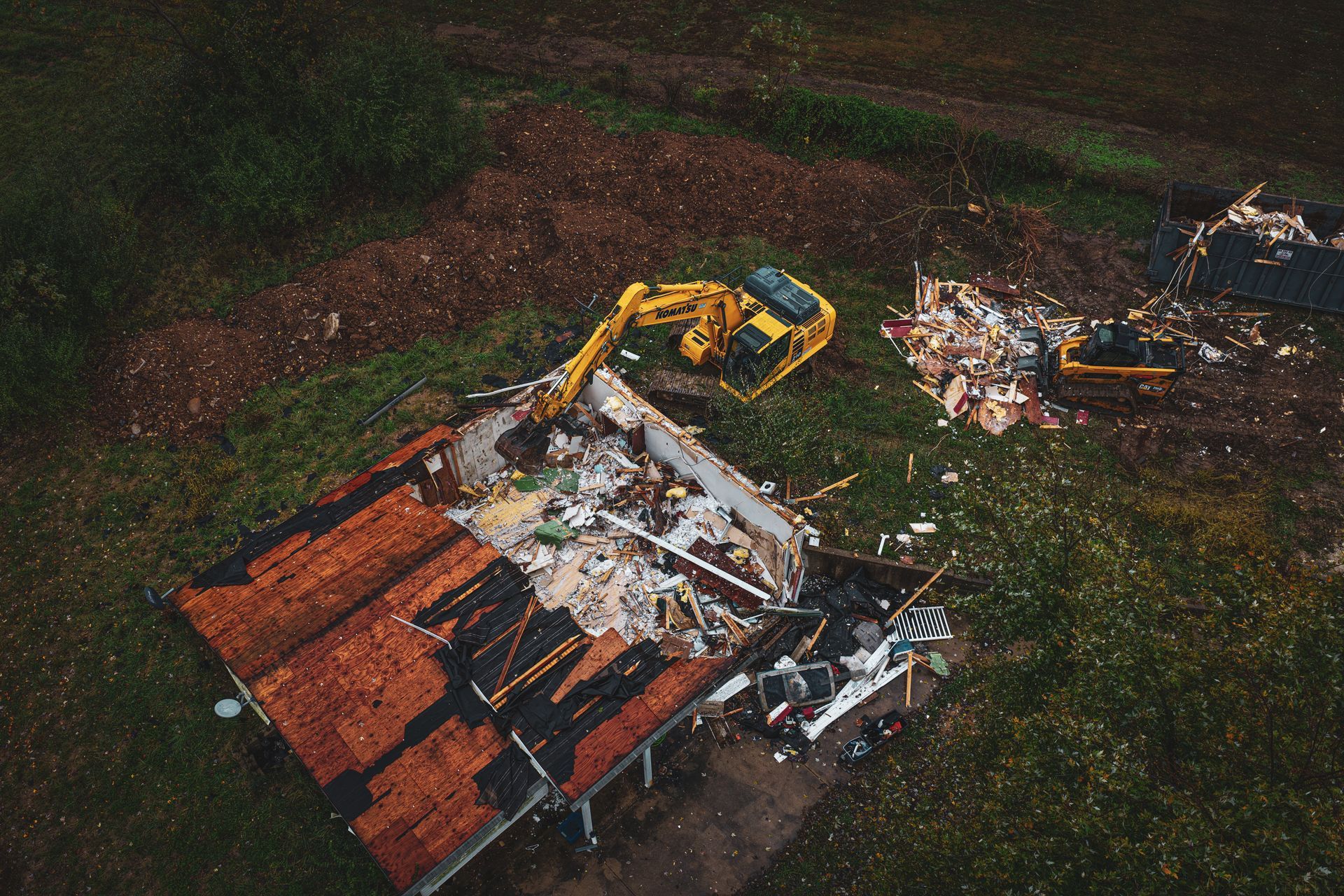Aerial view of a demolition site with a yellow excavator tearing down a collapsed building amid debris.