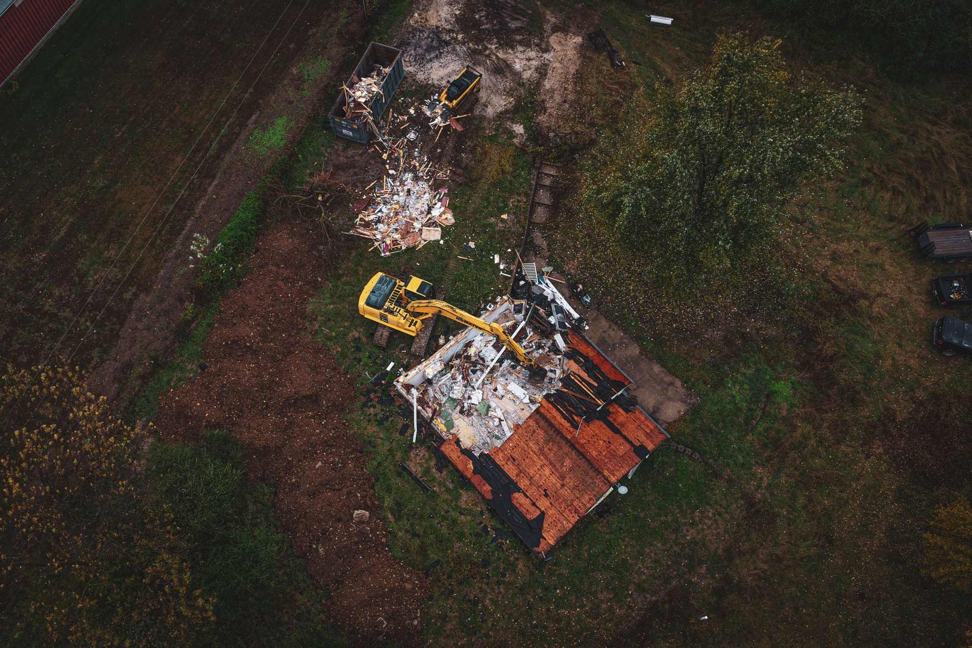 Aerial view of a burned-out yellow excavator beside charred debris on a grassy field