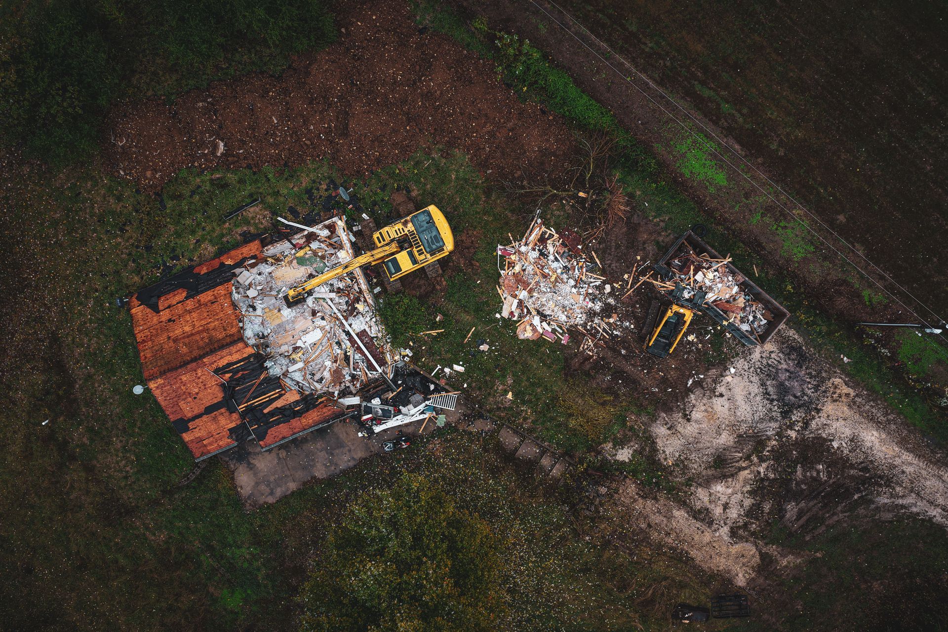 Aerial view of two yellow excavators amid rubble and debris on a cleared dirt lot
