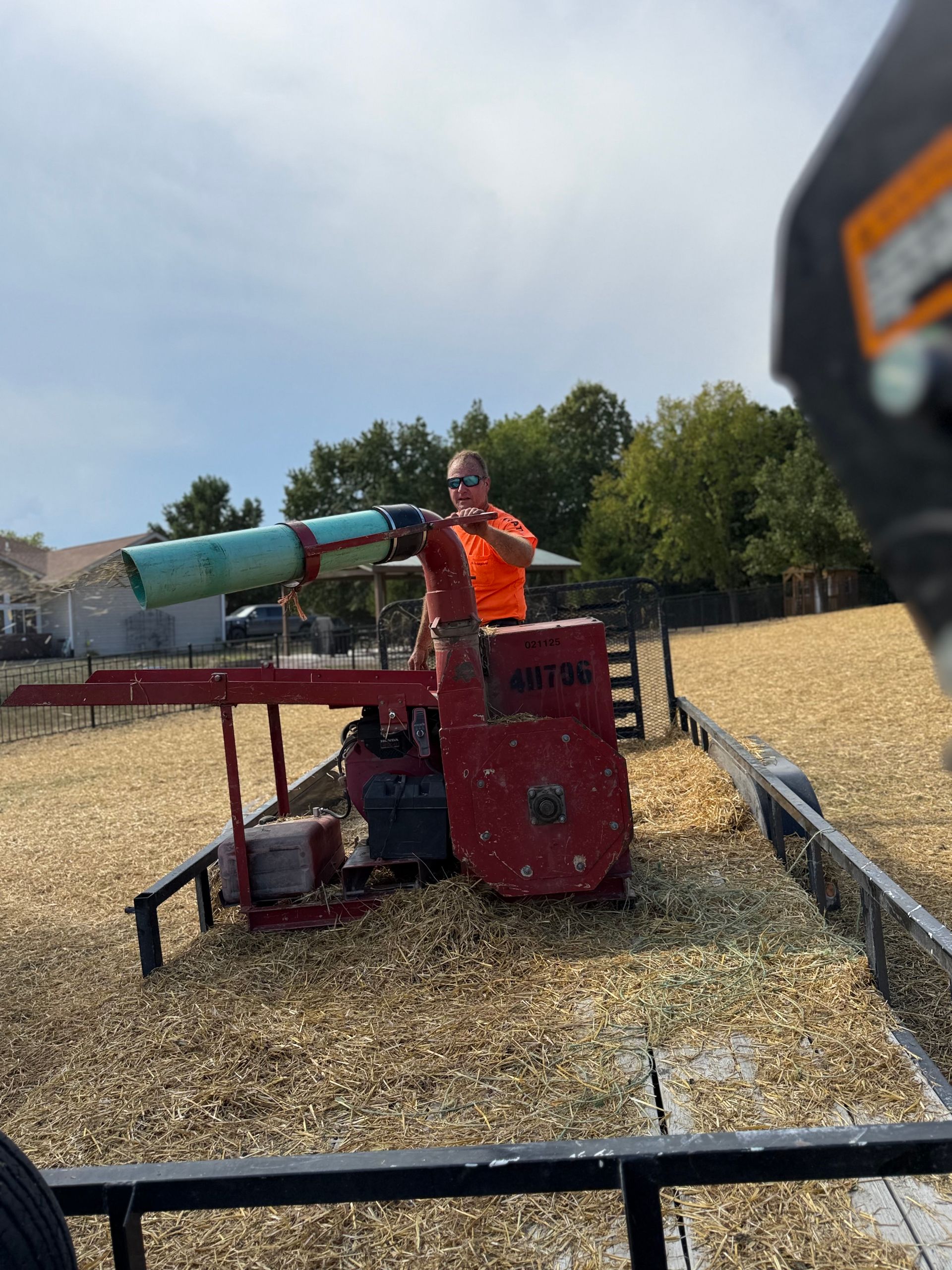 Person in orange operating a red industrial machine in a wood-chip yard under a sunny sky