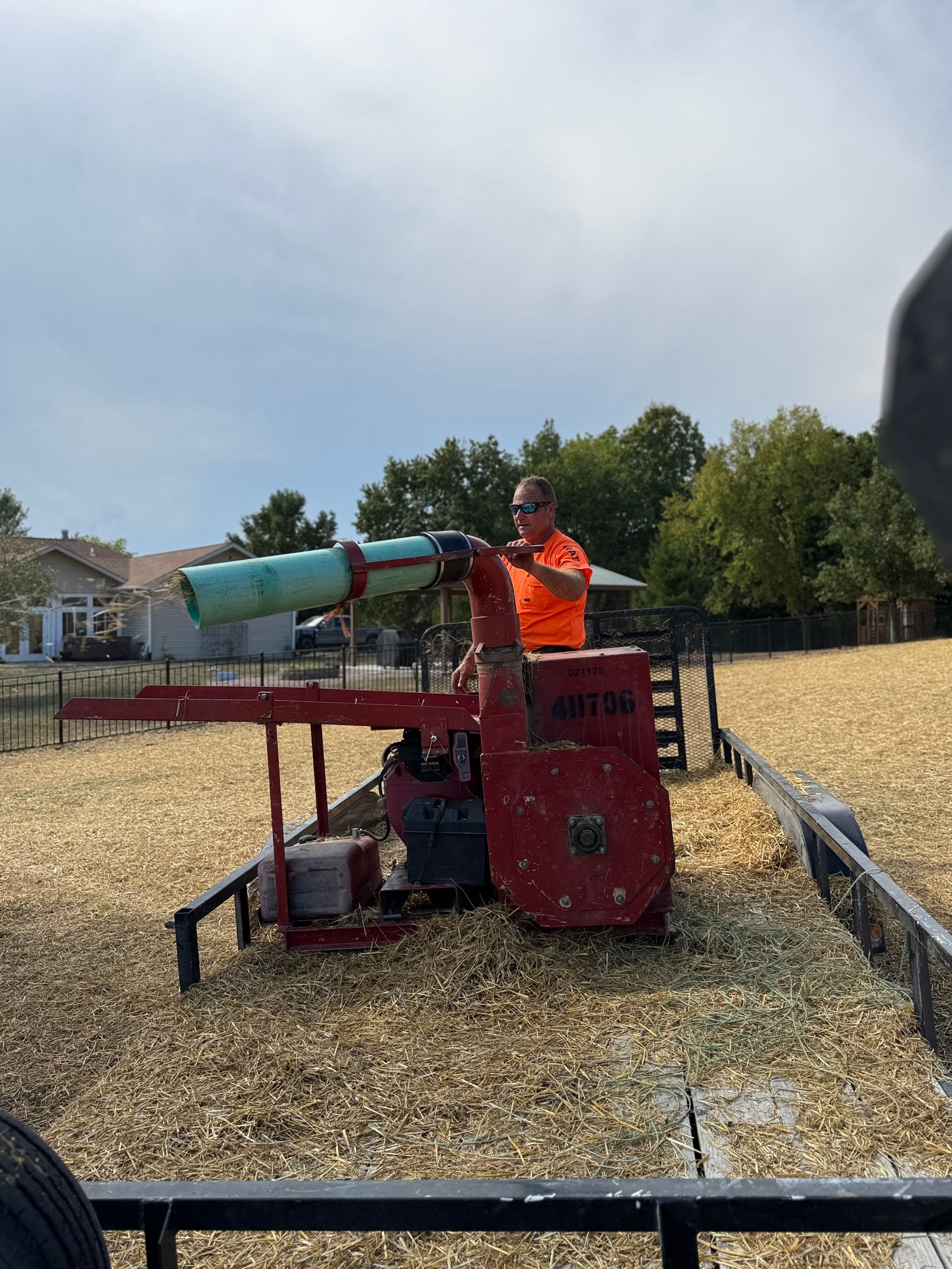 Worker in orange vest operating a red farm machine in a field of harvested crops under a cloudy sky