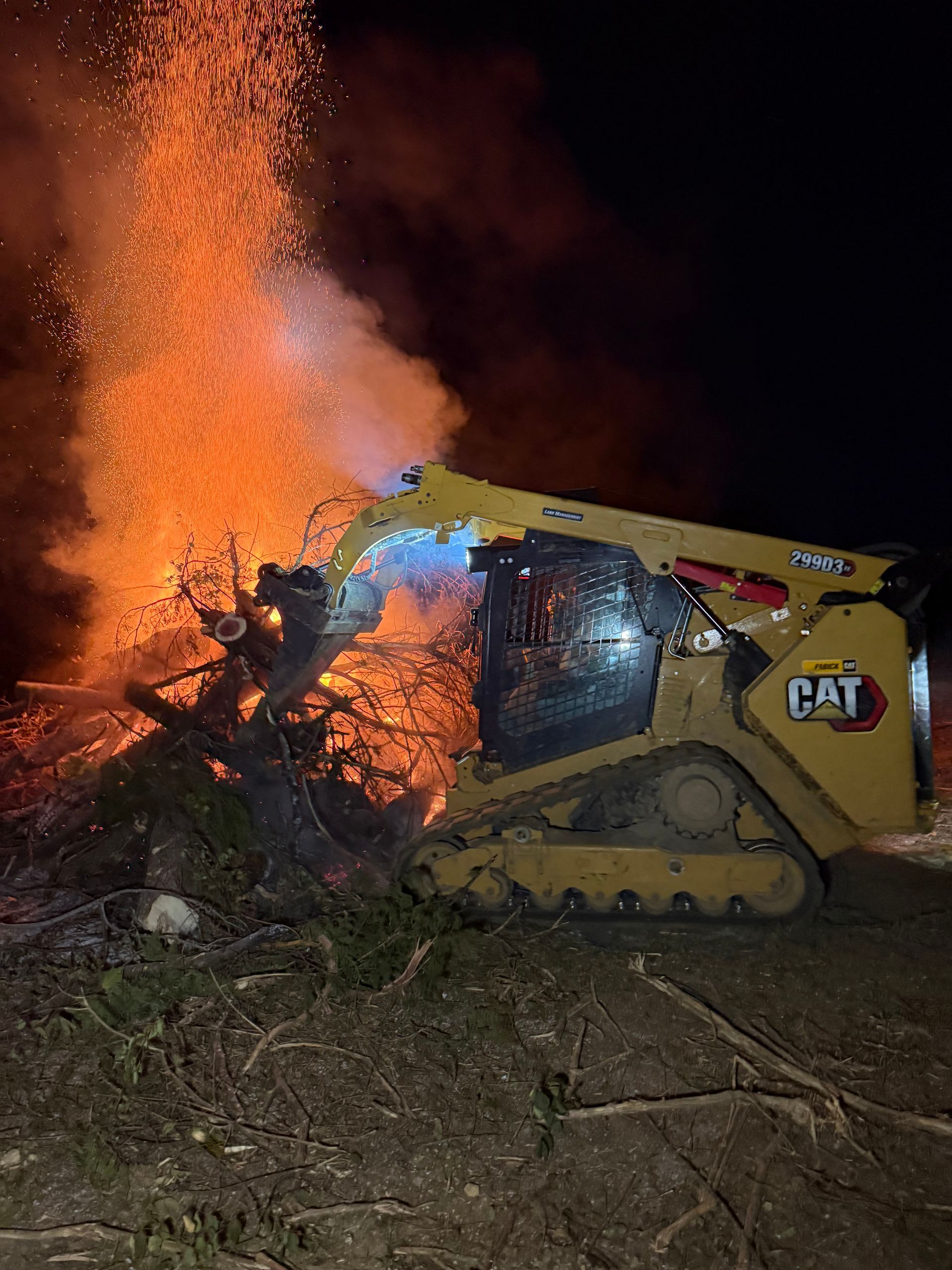 Yellow CAT bulldozer pushing brush at night beside a large orange fire and smoke
