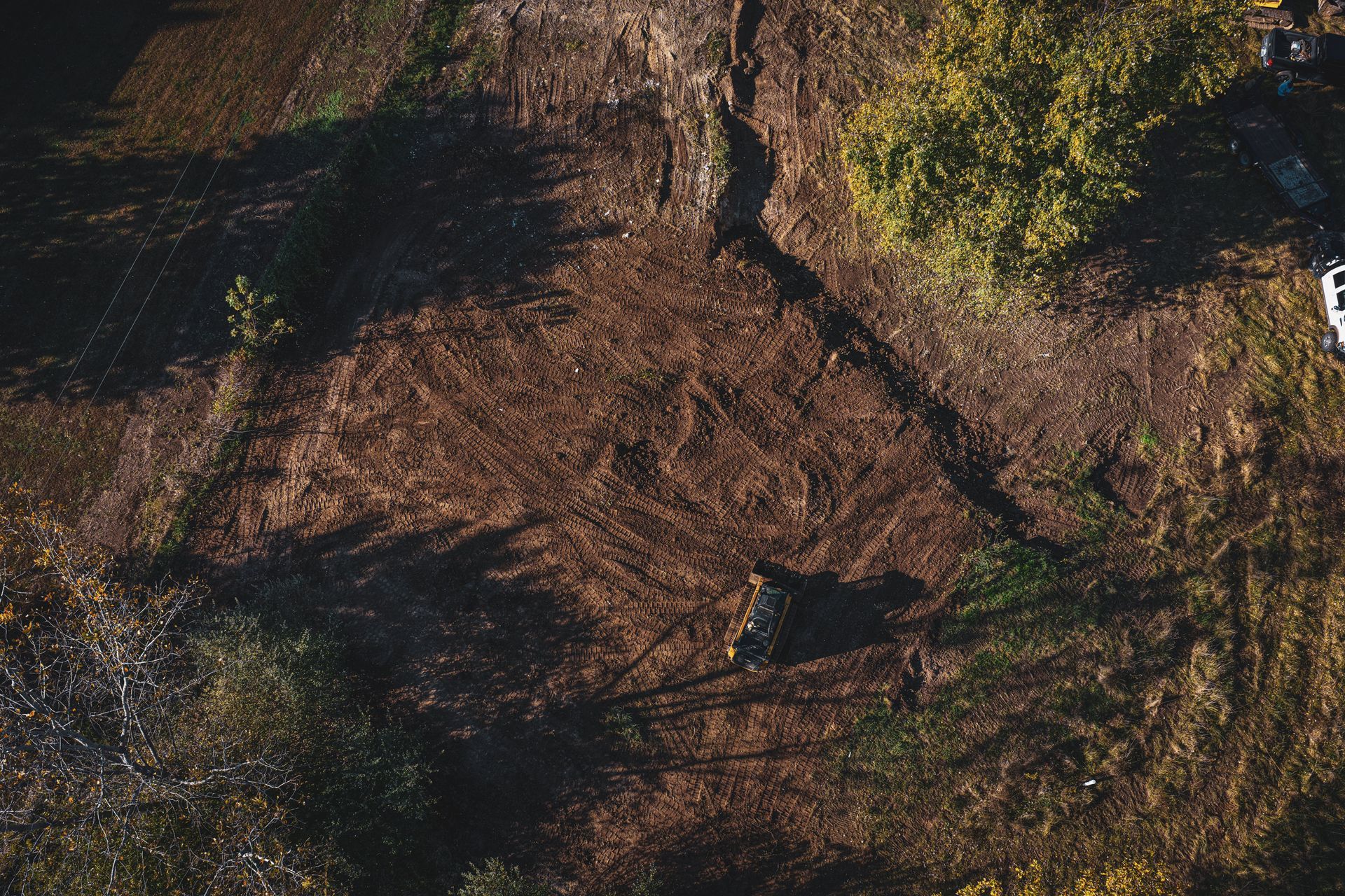Aerial view of a brown dirt path winding through dark trees and green shrubs.