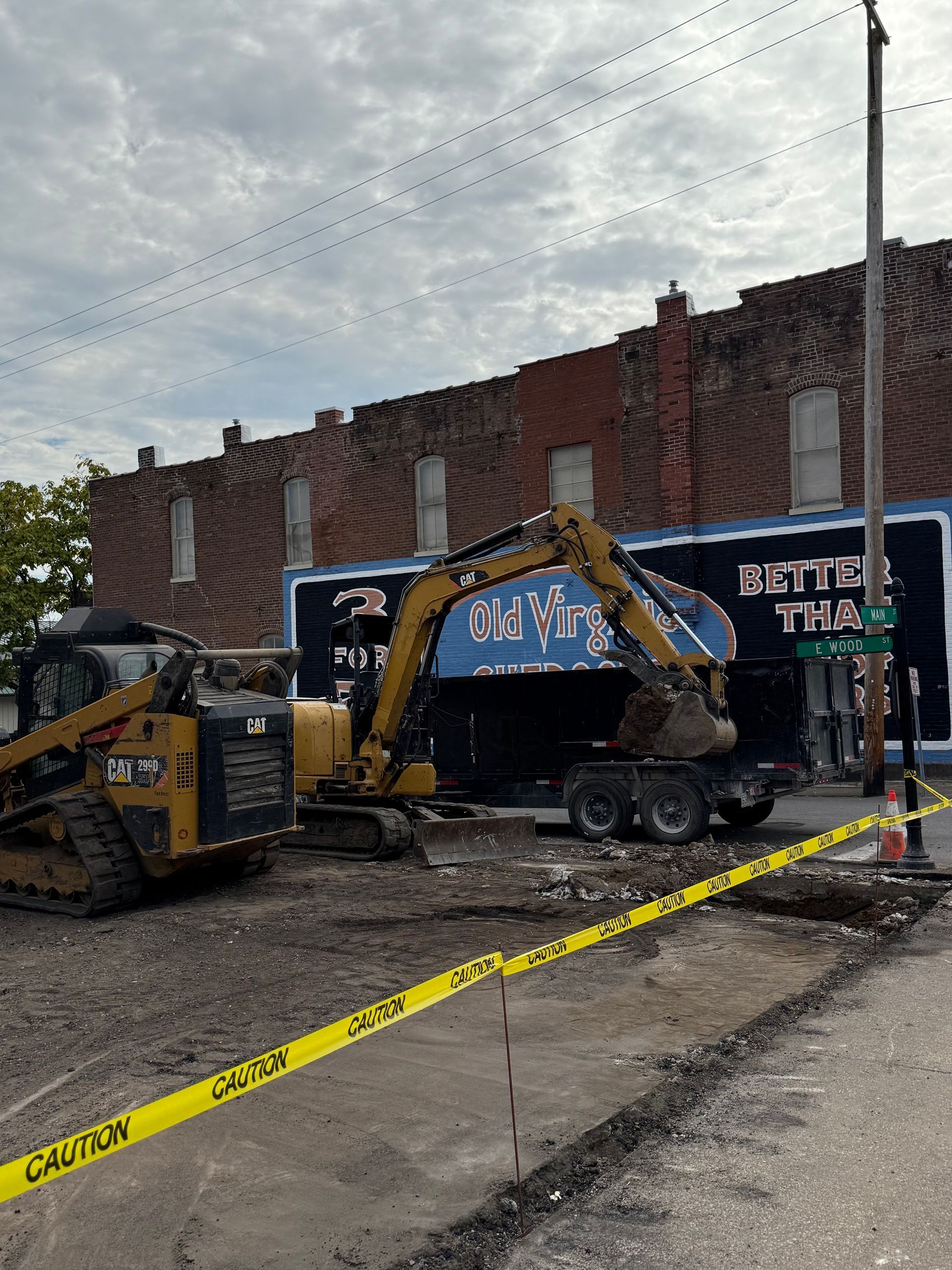 Construction equipment behind caution tape beside a brick wall and mural on a city street.
