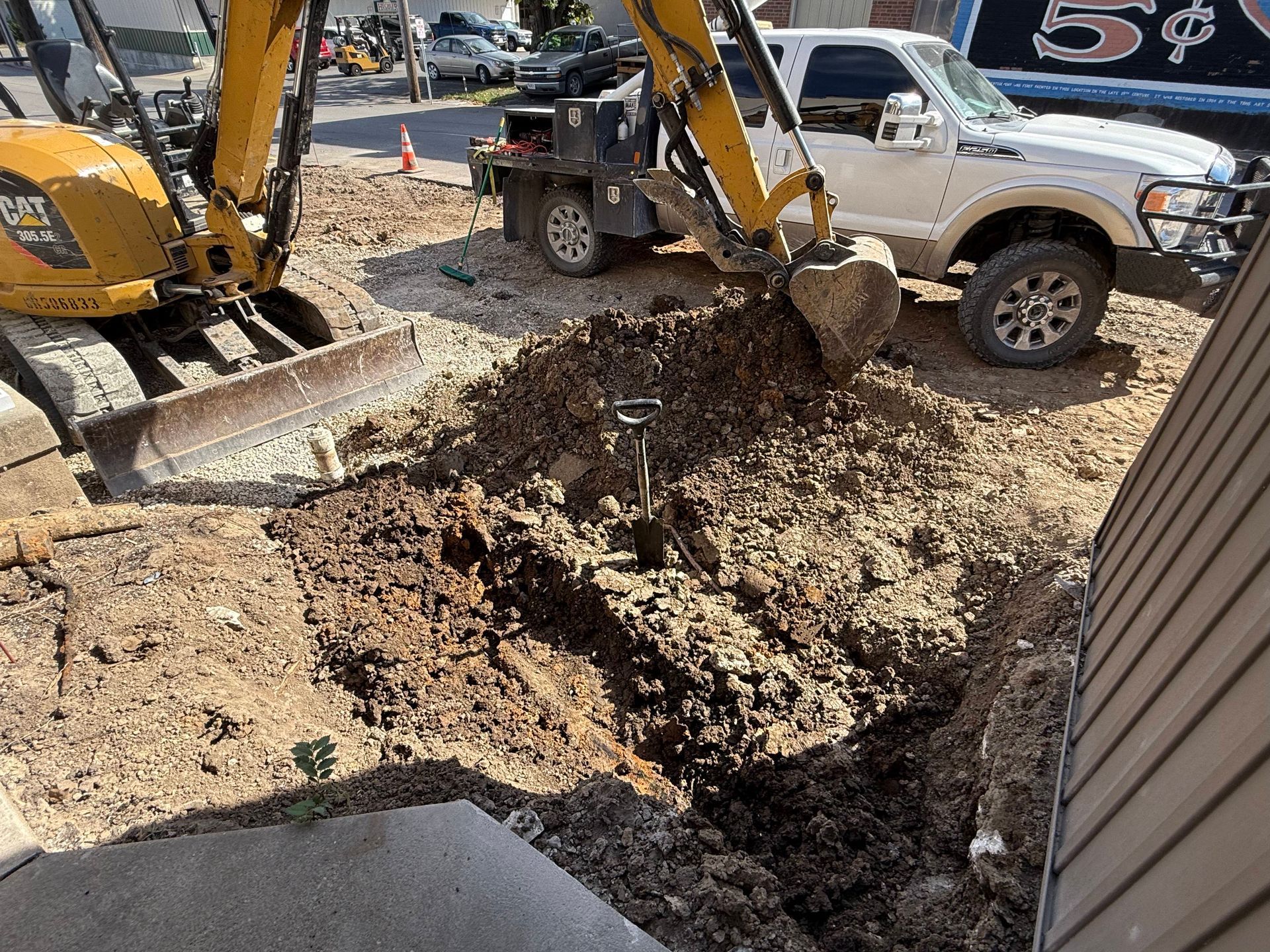 Backhoe digging a trench beside parked trucks at a construction site