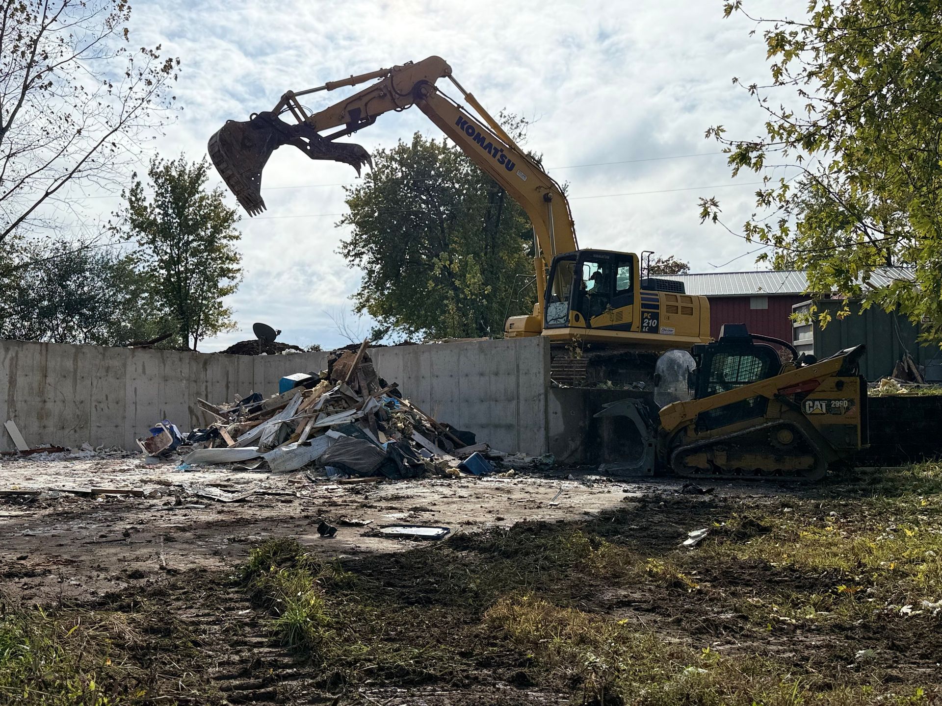 Excavator demolishing rubble behind a concrete wall in a construction site