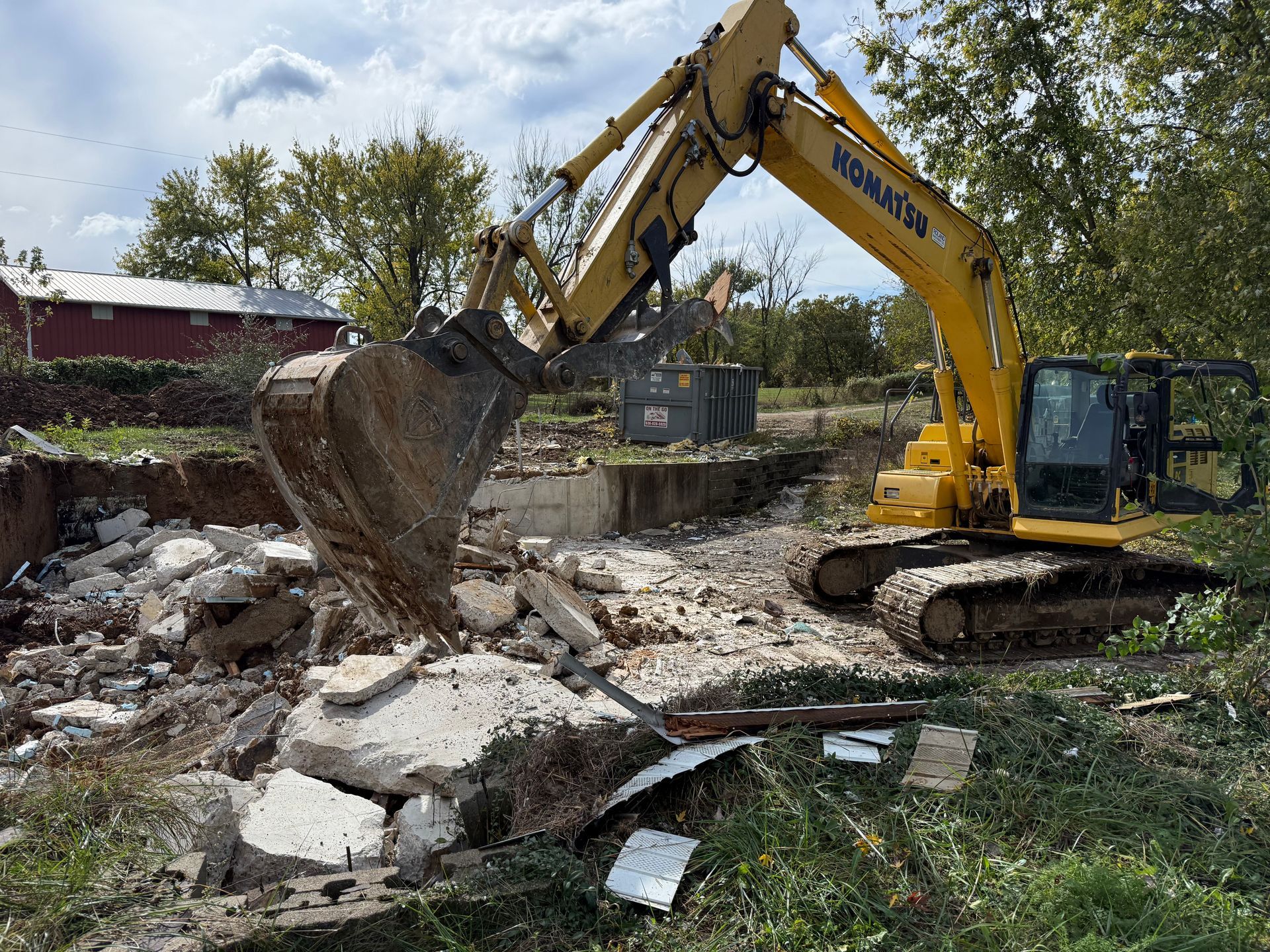 Yellow excavator demolishing rubble at a construction site under a cloudy sky