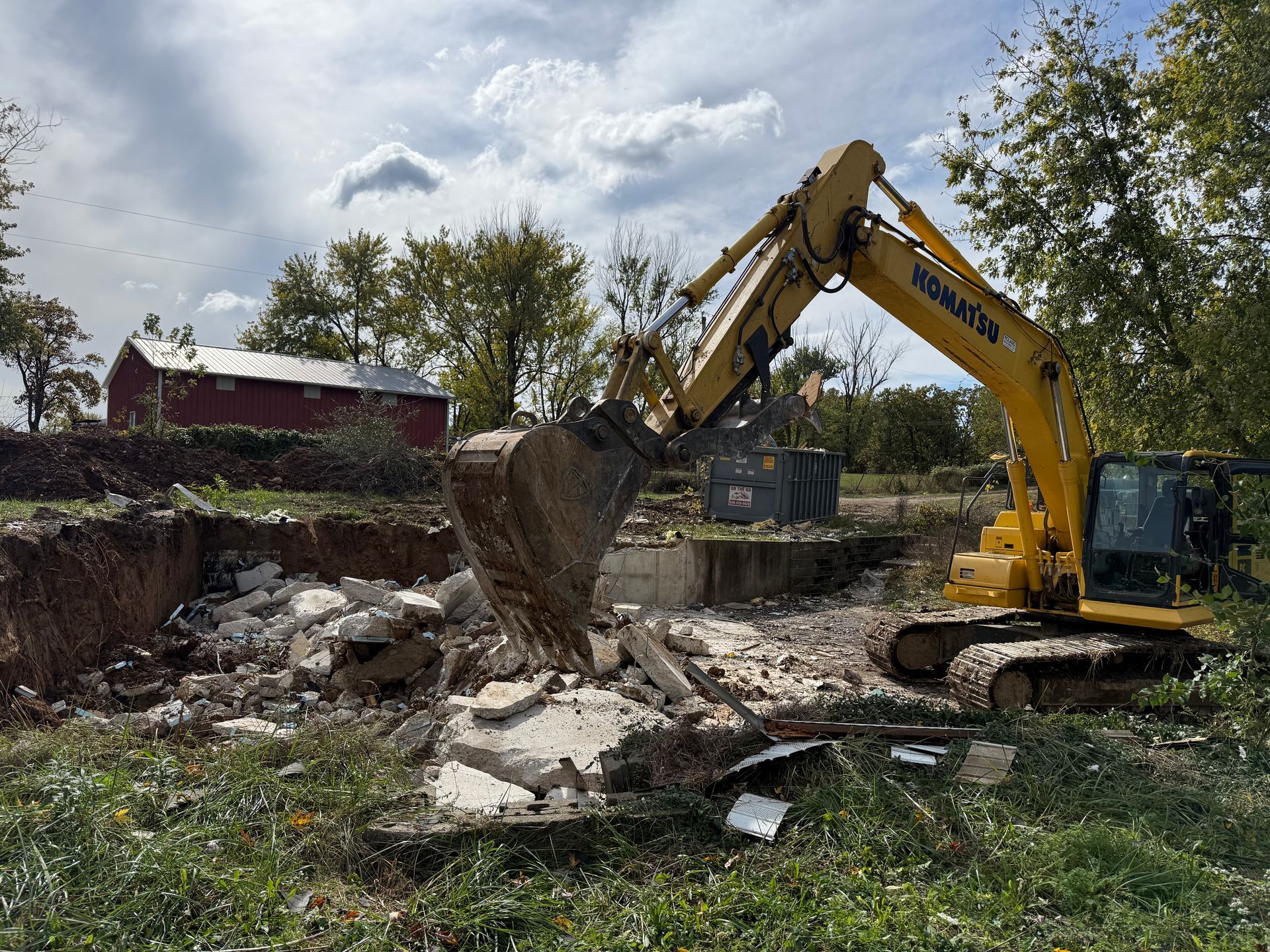 Yellow excavator digging rubble at a construction site under a partly cloudy sky.